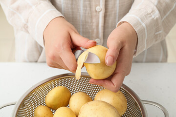 Woman peeling raw potatoes at table in kitchen, closeup