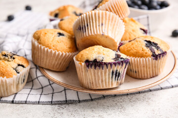 Plate with tasty blueberry muffins on light background
