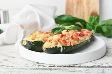 Plate with quinoa stuffed zucchini boats on light wooden background
