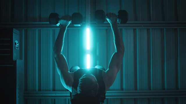 A Man Bench-pressing Weights In A Room With Blue Lights Around Him. A Person Working Out Doing Exercise At Home In A Dark And Moody Setting.
