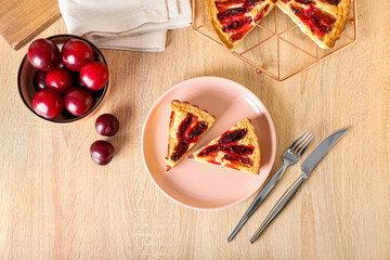 Plate with pieces of tasty plum pie on wooden background