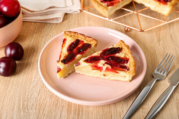 Plate with pieces of tasty plum pie on wooden background, closeup