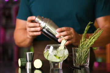 Male bartender making cucumber gin and tonic on table in bar