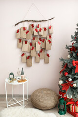 Advent calendar hanging on color wall in room with Christmas tree