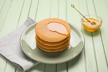 Plate of tasty pancakes with honey on color wooden background