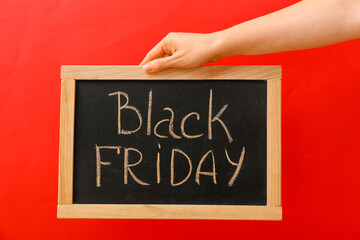 Female hand holding chalkboard with text BLACK FRIDAY on color background