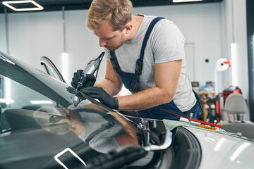 Car service technician checks crack on car windshield closeup