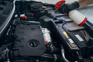 Mechanic in gloves clean car engine with spray at auto service station