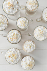 Glasses and cups of tasty latte with nuts on white wooden background