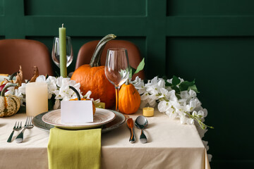 Autumn table setting with fresh pumpkins and flowers near green wall