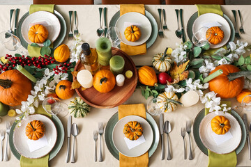 Autumn table setting with fresh pumpkins and flowers in room