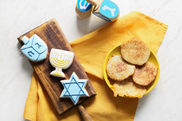 Tasty cookies and potato pancakes for Hanukkah celebration with dreidels on white background
