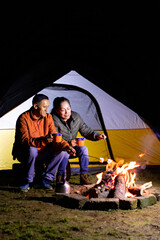 Obraz na płótnie Canvas A couple camping, holding cups in front of a campfire