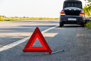 Red emergency stop sign (red triangle warning sign) and broken car on road