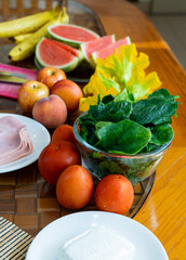 table with a plate of spinach, tomatoes, peaches, bread and ham.