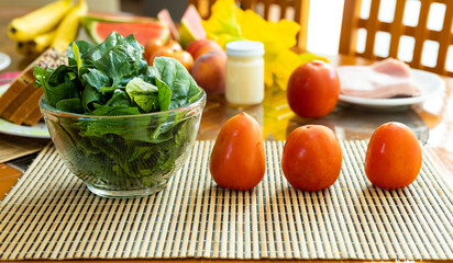 bowl of spinach with tomatoes on one side of the bowl, on a wooden table