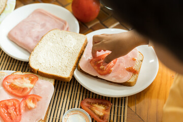 hands of a small child putting tomato slices in a sandwich