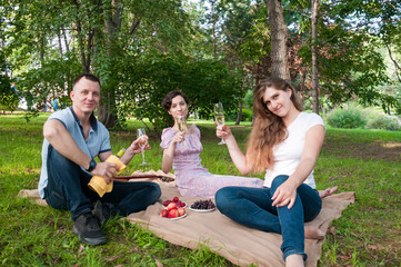 Two girls and a man are having a picnic in the summer in the park