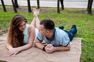 A young couple a guy and a girl are resting on the grass lying in the park in the summer