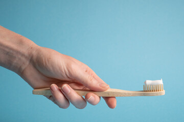 Hand holding bamboo toothbrush on blue. Holding wooden eco toothbrush. Natural toothpaste on a...