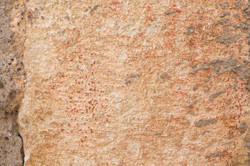 Beige and orange big stone block of wall with cement and red paint dots. Background and wallpaper textured picture. Copy space. Natural construction material. Sandstone building. 