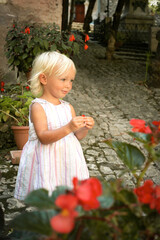 Beautiful blond blu eye caucasian baby girl in light summer dress with red flowers. Summer dreams concept. Childhood and travelling. Kid in old town. Positive emotions