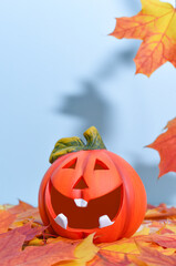 Funny lantern pumpkin with a smiling face on a blue background with maple leaves. Happy Halloween or Thanksgiving concept with copy space.