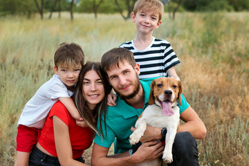 Family of Four Having Fun Playing with Purebred Beagle Dog In Rural Settings. Authentic group people portrait. Animals and friendship. Life in the Countryside