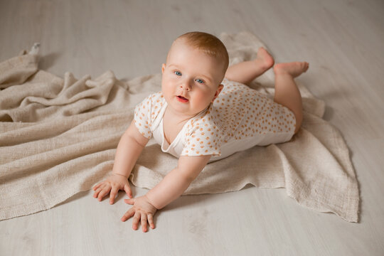 cute baby in a bodysuit is lying on his stomach on the wooden floor with a blanket at home. High quality photo