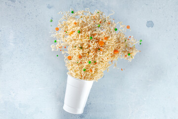 Ramen cup with instant noodles flying out of it, fast food levitation. Noodle meal with carrot and...
