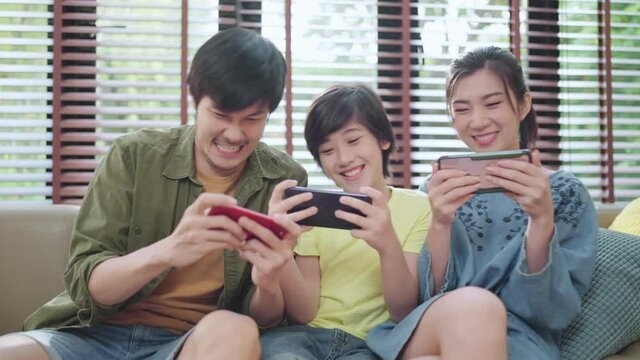 family quality time,asian parent and son sit relax playing game console or smart together laugh joyful smiling on sofa couch in living room at home,asian family homs isolation quarantine ideas concept