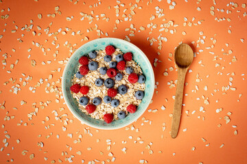 Healthy breakfast - oatmeal with blueberries and raspberries on orange background. Flat lay