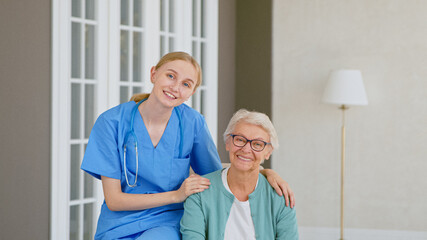 Obraz premium Pretty young doctor with stethoscope hugs smiling senior woman patient posing for camera