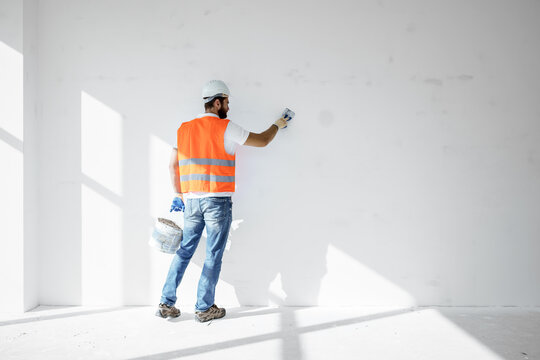 Plasterer in workwear smoothing wall surface of building indoors