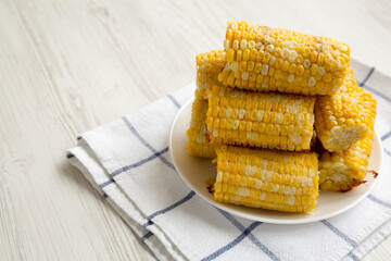 Homemade Butter Parmesan Corn on a white plate on a white wooden surface, side view. Copy space.