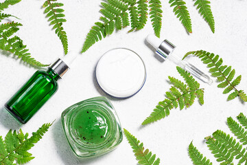Set of natural herbal cosmetic such as serum, face cream and scrub on white marble background with fresh green fern leaves top view. Skin care concept.