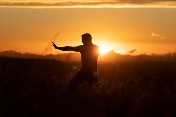The silhouette of a young man, performing martial arts postures, formed by the last orange sun...