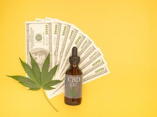 Top view of cannabis leaf on dollar banknotes and a CBD oil bottle isolated on a yellow background...