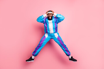 Photo of funny impressed dark skin man wear blue suit headband jumping high arms head smiling isolated pink color background