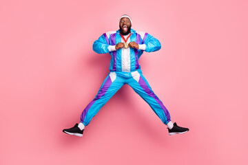 Fototapeta na wymiar Photo of lucky excited dark skin guy dressed sport suit headband smiling holding gold medal jumping isolated pink color background