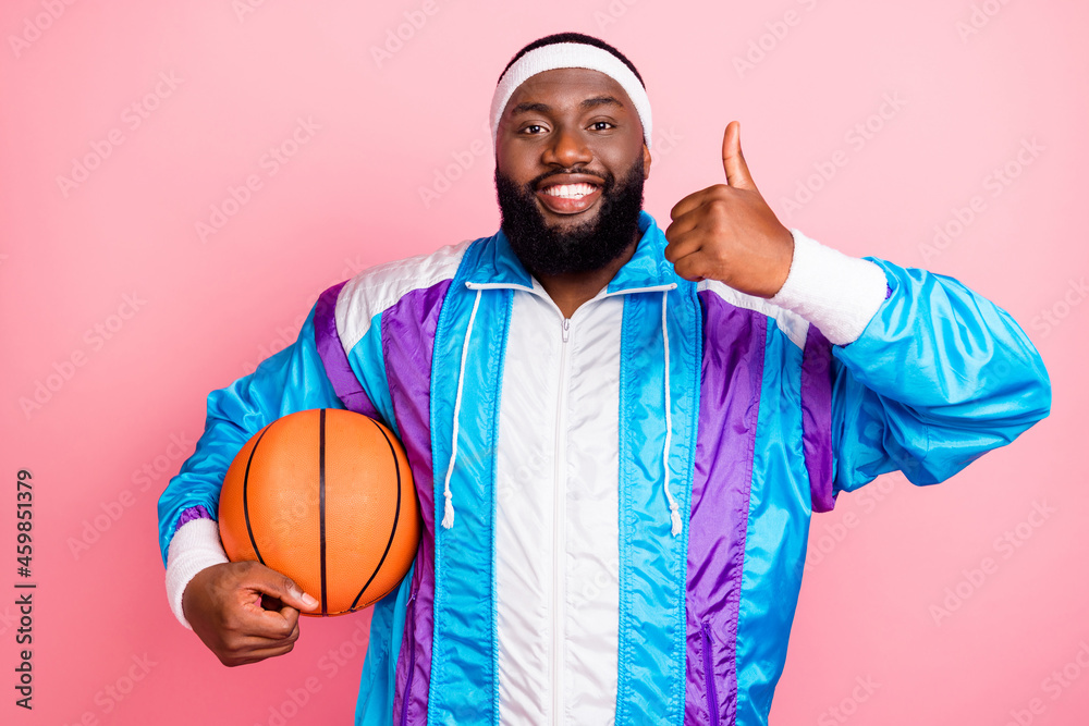 Wall mural Photo of pretty charming dark skin guy dressed sport suit headband basketball showing thumb up isolated pink color background