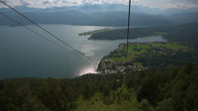 View from cable car of the Herzogstandbahn riding down to the mountain lake Walchensee while passing other gondola on sunny day