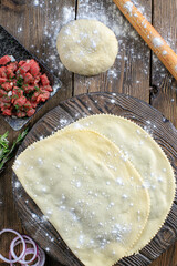 Frozen chebureks on a wooden board on grey table with ingredients. Traditional homemade food. Top view. Copy space