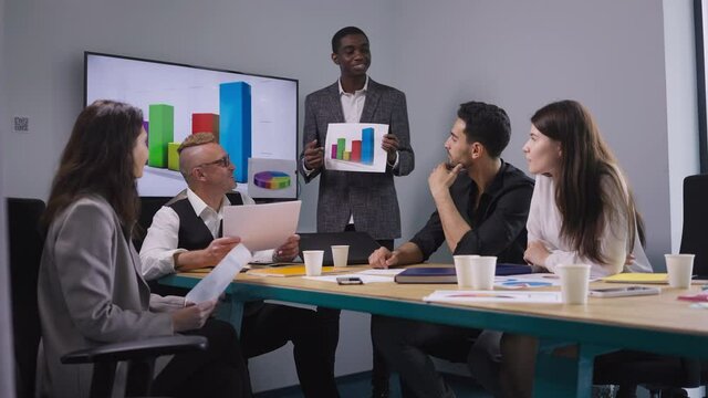 Portrait of expert African American man presenting business strategy idea with colleagues endorsing coworker smiling talking. Professional manager brainstorming in office with employees