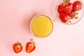 Fresh strawberries in a plate with a glass of orange juice on pink table, copy space, top view