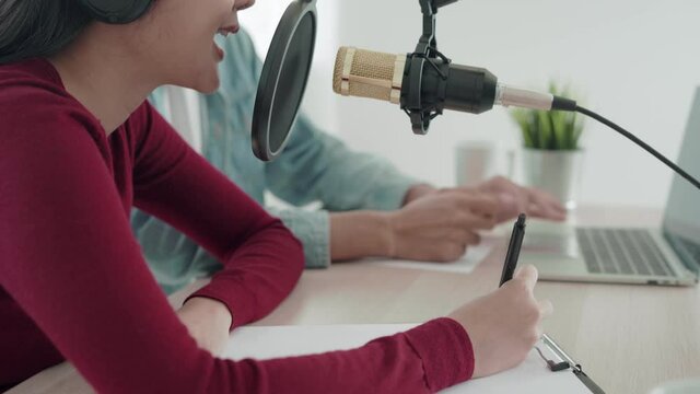 woman was speaking on a morning radio station broadcasting a news program and men preparing the content via computers. The woman is testing the microphone by speaking test. concept podcast .
