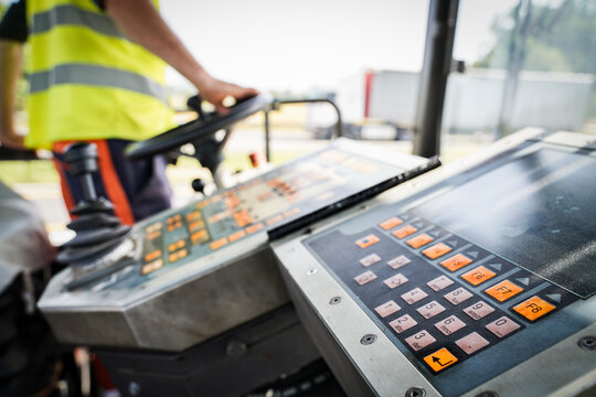 Worker operating asphalt paver machine during road construction with control panel up-close