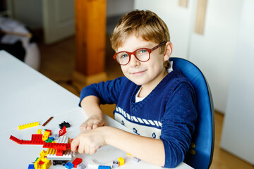 Little blond child with eye glasses playing with lots of colorful plastic blocks. Adorable school...
