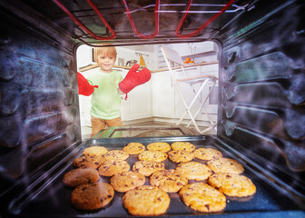 Blond boy with oven-gloves check cookies in oven