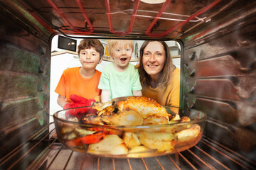 Mother and two boys take roasted chicken from oven